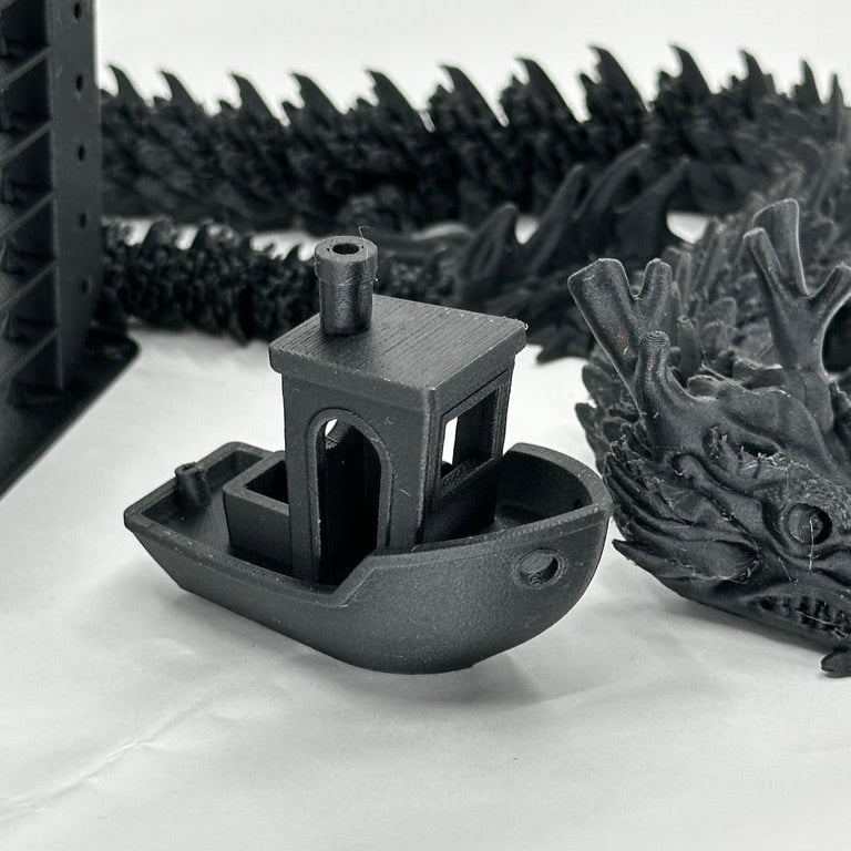Black 3D-printed model of a boat and dragon on a white surface